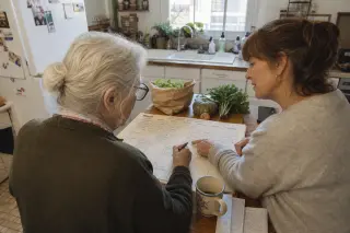 Senior woman and neighbor updating a wall calendar together in a cozy Nantes kitchen, sunlight softly filling the room.