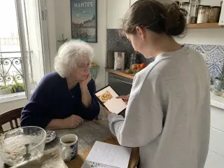 Senior woman and teenage girl sharing a quiet cooking moment in a sunlit Nantes kitchen, focused on a tablet together.