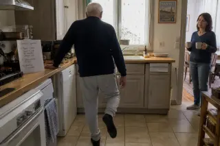 Senior man in a Nantes kitchen doing a gentle balance exercise with his daughter nearby, morning light, calm homely atmosphere.