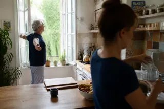 Senior man stretching by kitchen window with a mid-aged woman in background, natural bright light, serene domestic scene in Nantes.