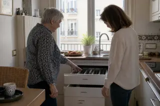 Senior woman and daughter talking quietly in a sunlit Nantes kitchen, showing accessible cupboards amid homely kitchen details.
