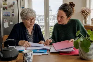 Senior woman and her adult daughter sorting documents together at a kitchen table in a naturally lit Nantes apartment, focused on their hands and subtle connection.