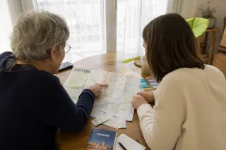 Senior woman and adult daughter planning an outing at a dining table with a Nantes map and natural daylight, candid atmosphere.