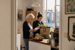 Senior woman and her daughter unpacking groceries together in a cozy Nantes kitchen, natural light, warm and authentic everyday interaction.