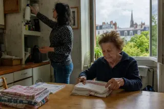Senior woman folding laundry with help from a middle-aged woman in a cozy Nantes kitchen, warm natural light, candid moment